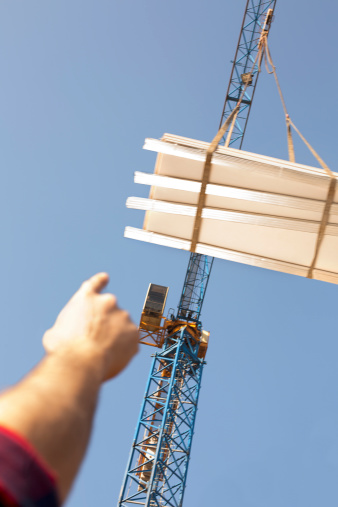 Construction worker's finger is pointing a load hold by a crane. Motion blur.