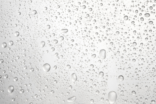 Drops of rain on glass against blue sky and white clouds.