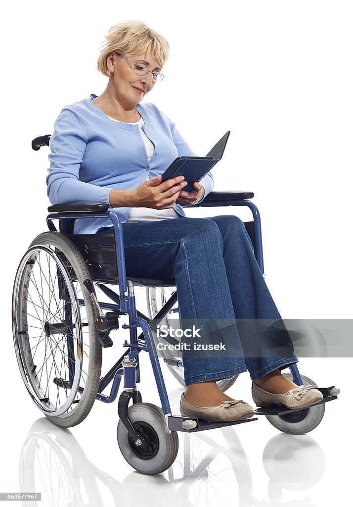 Mature woman in wheelchair Portrait of mature woman sitting in wheelchair and reading an e-bookt. Studio shot on white background. Wheelchair Stock Photo