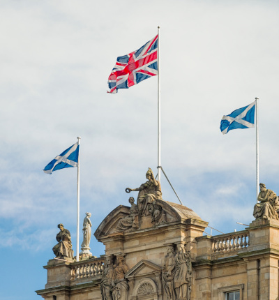 Two Scottish Saltire flags flying on either side of a Union Flag on the top of a building in Edinburgh.