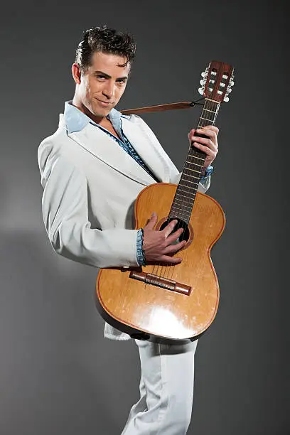 Photo of Retro rock and roll male guitar player wearing white suit.