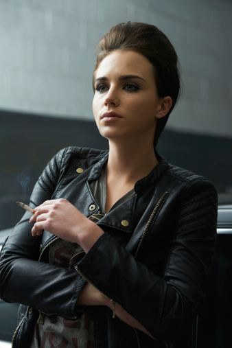 Shot of a rebellious looking young woman smoking a cigarette in a car garage