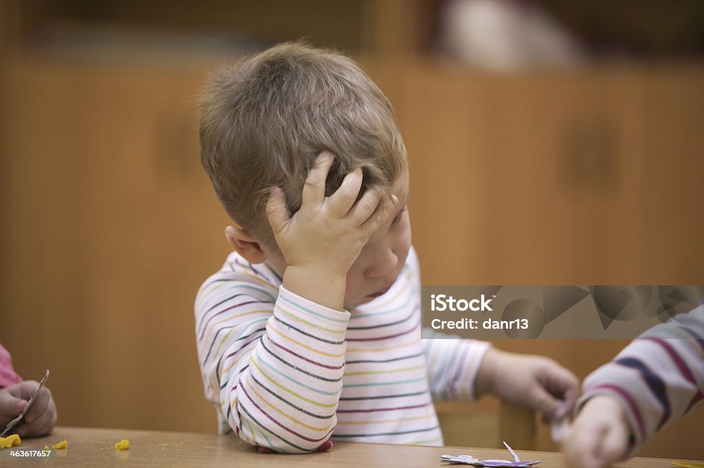 Cute little child in kindergarten class Cute little boy in kindergarten class sitting with his head resting on his hand watching the child alongside writing or drawing Animal Body Part Stock Photo