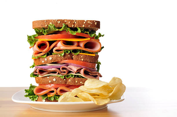 Triple Decker Dagwood Sandwich on Whole Wheat Bread Horizontal image of a triple decker dagwood sandwich and a side of potato chips sitting on a white plate. dagwood stock pictures, royalty-free photos & images