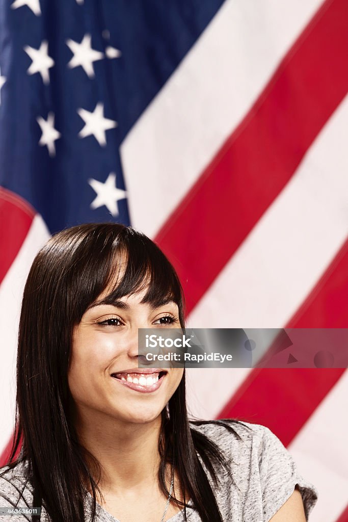 Proud young American girl smiling by Stars & Stripes A cheerful, confident-looking young woman with long, dark hair smiles happily in front of the Stars & Stripes - the US national flag. A pretty patriot! Politics Stock Photo