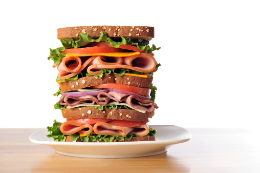 Horizontal image of a triple decker dagwood sandwich sitting on a white plate with a white background.
