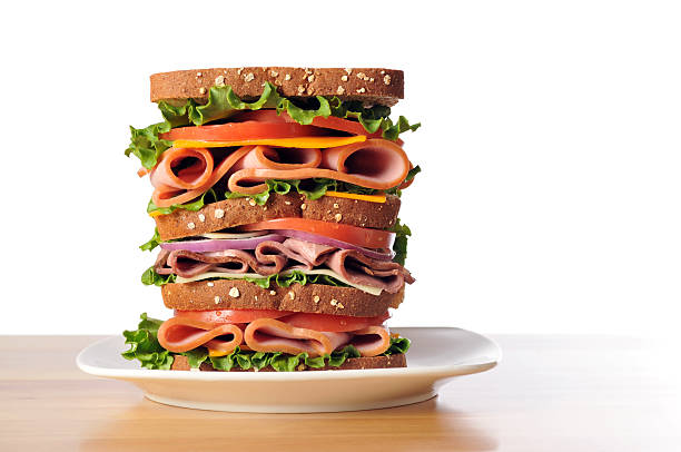 Triple Decker Dagwood Sandwich on Whole Wheat Bread Horizontal image of a triple decker dagwood sandwich sitting on a white plate with a white background. dagwood stock pictures, royalty-free photos & images