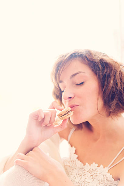 istock Young woman eating macaron with delight, backlit. 463662753