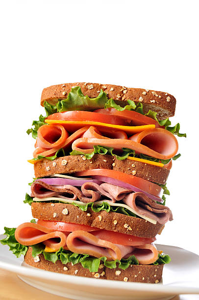 Triple Decker Dagwood Sandwich on Whole Wheat Bread Vertical image of a triple decker dagwood sandwich sitting on a white plate. Low camera angle accentuates the height of the sandwich. dagwood stock pictures, royalty-free photos & images