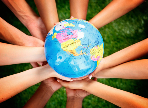 A large group of mixed hands cradle a world globe carefully. Environmental awareness but also travel or geography could apply here. The countries seen on the globe include North and South America.. 