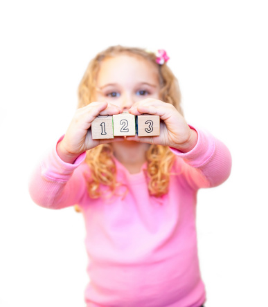 Young girl holding out a 1, 2 and 3 wooden block in front of her.