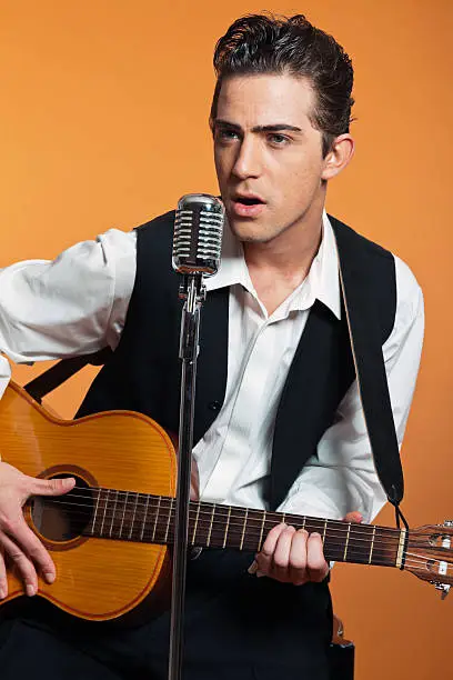 Photo of Retro country singer with guitar wearing black suit. Studio shot.