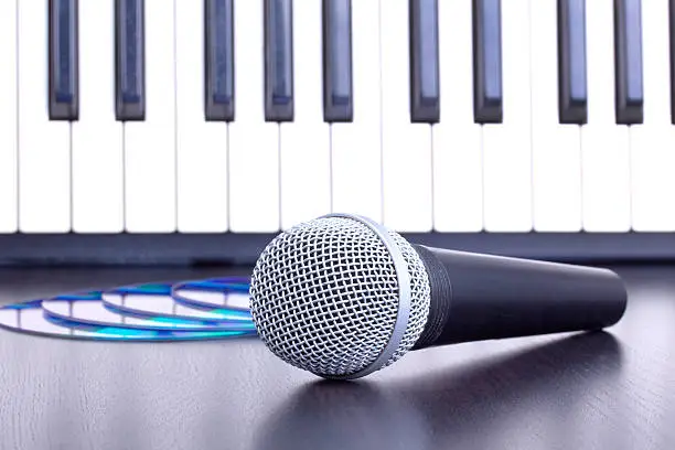 Photo of Microphone, cd disks and piano keyboard on black table