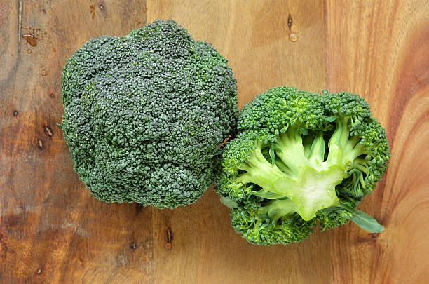 Broccoli crowns Fresh washed broccoli crowns on rustic wooden cutting board broccoli crowns stock pictures, royalty-free photos & images