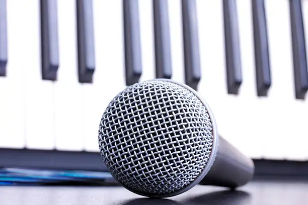 Photo of Microphone and piano keyboard on black table