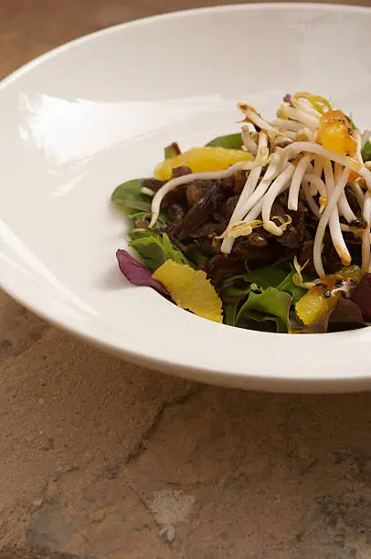 Crispy duck salad with orange, beansprouts and figs served in a white bowl.