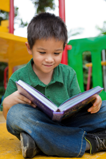 Happy little boy reading and studying his book outside in the playground. You can homeschool anywhere!