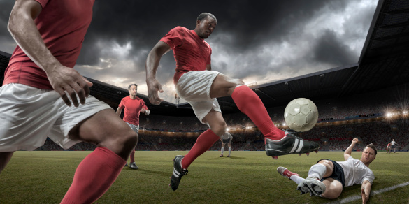 Mid air action of professional football player about to strike ball during game in floodlit stadium full of spectators under cloudy evening sky