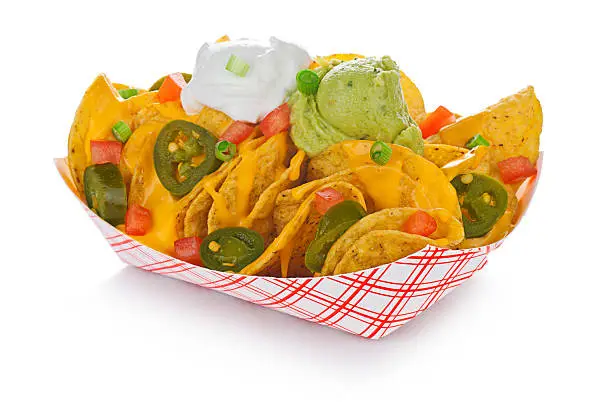 Super-deluxe nachos with jalapenos, sour cream, guacamole, tomatoes and green onions in a standard restaurant paper tray.