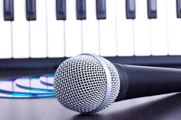 Photo of Microphone, cd disks and piano keyboard on black table