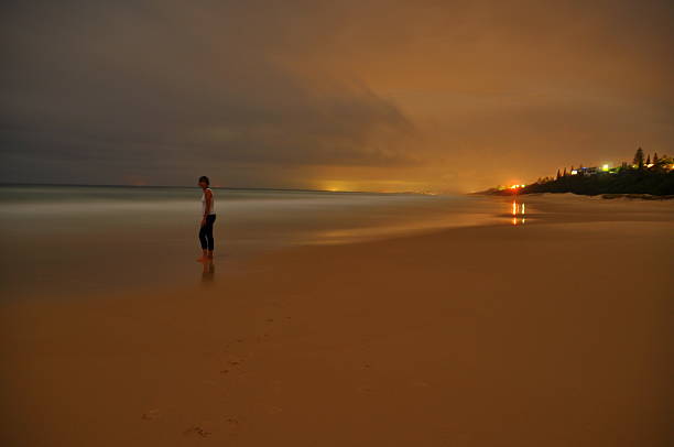 Long exposure image showing the blurry silhouette of a young man standing on a beach at dusk