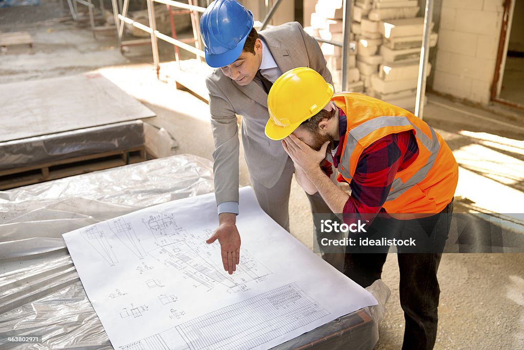 Failure Engineer and worker having a fight about plans. Construction Industry Stock Photo