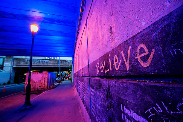 The wall along a covered walkway in Philadelphia has Believe written. Mixed lighting casts a strong pink color.