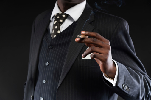 Close-up of hand of retro african american mafia man wearing striped suit and tie. Smoking cigar. Studio shot.