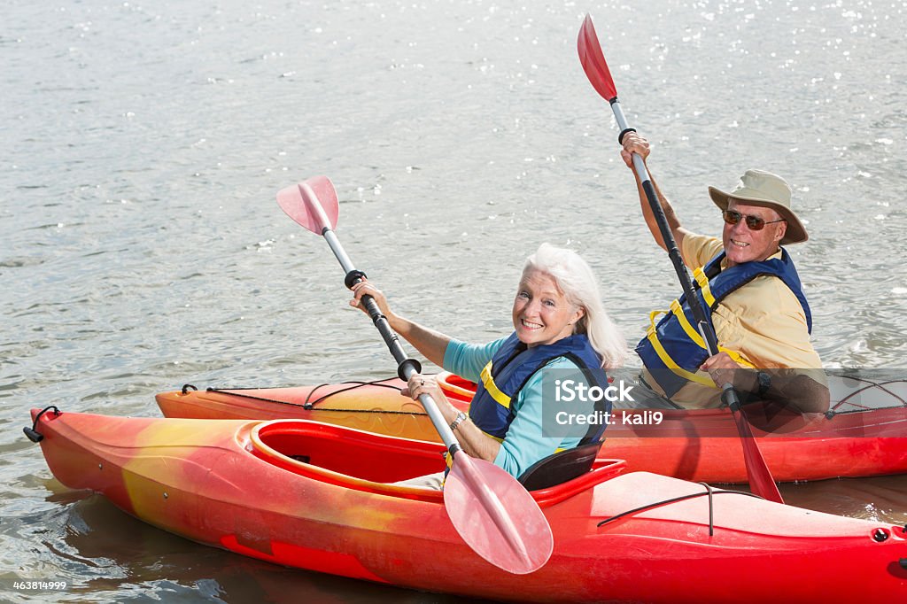 Senior couple kayaking Active senior couple with kayaks, looking over shoulder at camera. Kayaking Stock Photo
