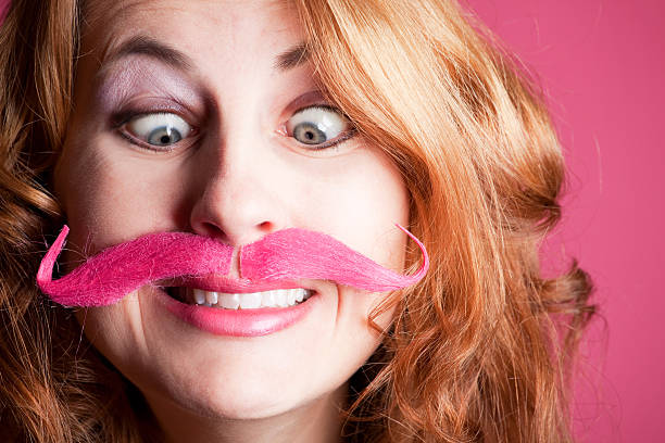 Smiling Woman With Pink Mustache A smiling woman wearing a pink handlebar mustache. women movember mustache facial hair stock pictures, royalty-free photos & images