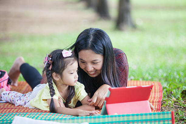 istock Asian mother & daughter laying on blanket playing on tablet 463851629