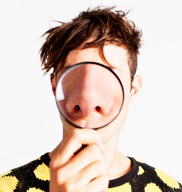 Magnifying glass enlarges young man's nose dramatically