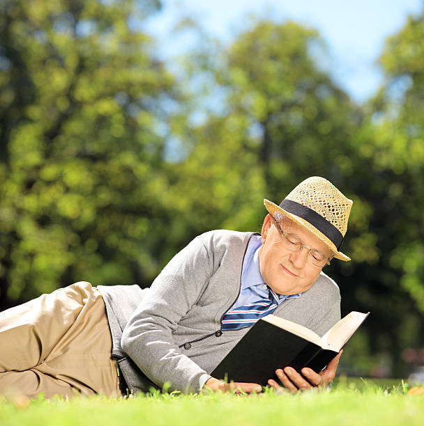 istock Senior man with hat lying on grass and reading 463866807
