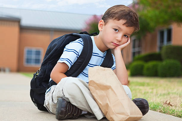 Young child sitting outside his school building Young child sitting outside his school building. food elementary student healthy eating schoolboy stock pictures, royalty-free photos & images