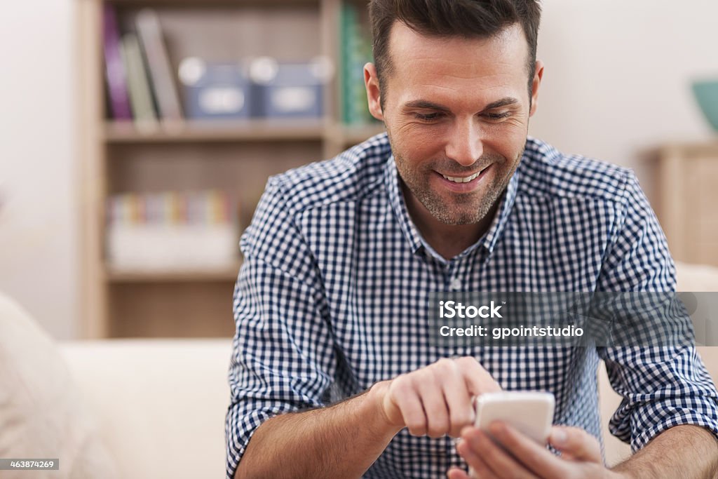 Happy man using mobile phone at home in living room Happy man using mobile phone at home in living room  Adult Stock Photo