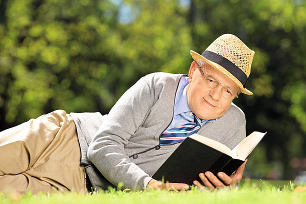 istock Senior gentleman lying on a grass with book in park 463875579