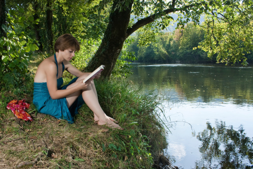 Beautiful young woman in a blue dress sitting by the river and read a bookeautiful young woman in a blue dress sitting by the river and read a book