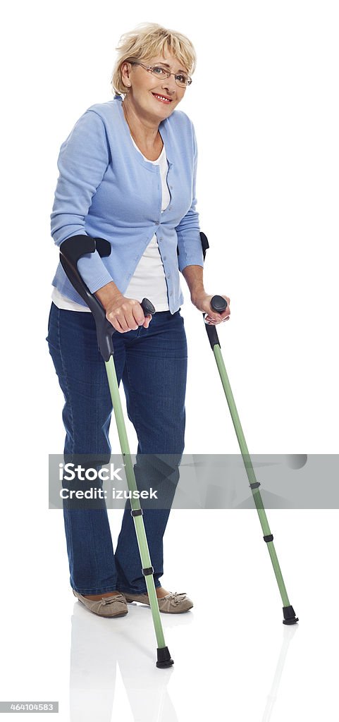Mature woman with crutches Full lenght portrait of smiling mature woman standing with crutches. Studio shot on white background. White Background Stock Photo