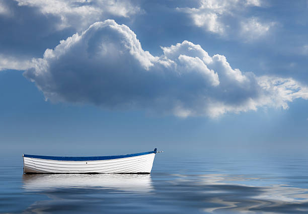 Old rowing boat marooned at sea Concept image of loneliness, lacking direction, no leadership, rudderless, floating, listless or generally adrift without a goal rowboat stock pictures, royalty-free photos & images