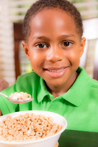 Food:  African descent little boy enjoying his breakfast cereal. African descent little boy has cereal for breakfast.  School or home setting.  boys bowl haircut stock pictures, royalty-free photos & images