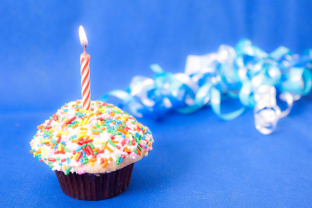 istock Cake: Birthday cupcake, one burning candle.  Blue background. 464179045