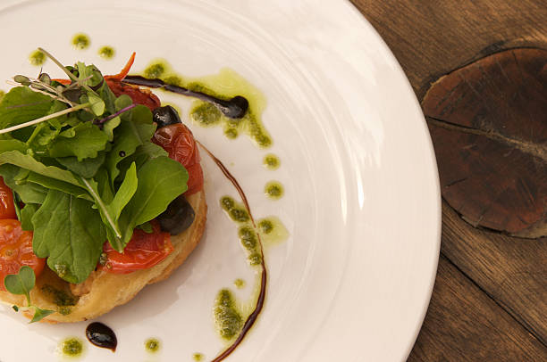 Tomato and olive tarte tatin with rocket salad, balsamic syrup and rocket pesto served on a white plate.