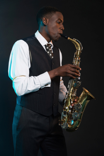 Retro african american jazz musician playing on his saxophone. Wearing suit and tie. Studio shot.