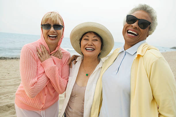 Three older woman laugh while on the beach Friends Laughing at Beach 50 59 years stock pictures, royalty-free photos & images