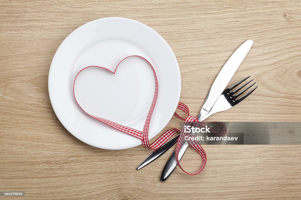 Valentine's Day heart shaped red ribbon over plate with silverware Valentine's Day heart shaped red ribbon over plate with silverware. On wooden table background Celebration Stock Photo