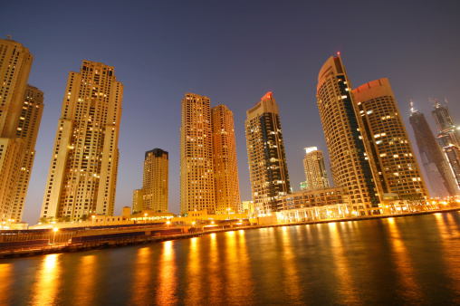 Tall high rise buildings in the Dubai Marina development, reflecting the golden hues of the lights across the water.