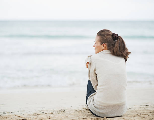 istock young woman wrapping in sweater while sitting on lonely beach 464308911