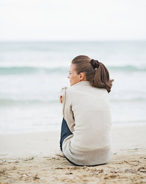 istock young woman wrapping in sweater while sitting on lonely beach 464308915