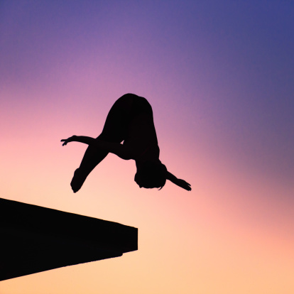 Silhouette of lady diver, diving from platform. Photographed at dusk against setting sun, colorful sky as background