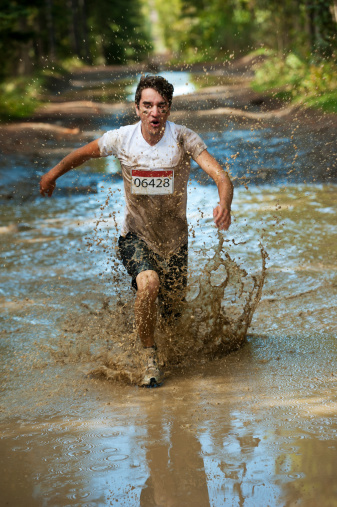 A racer in a mud race splashing though a puddle